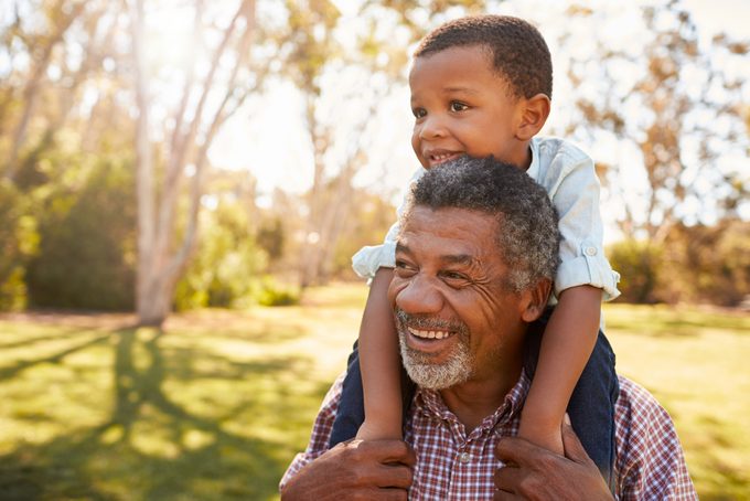 Grandfather,carries,grandson,on,shoulders,during,walk,in,park