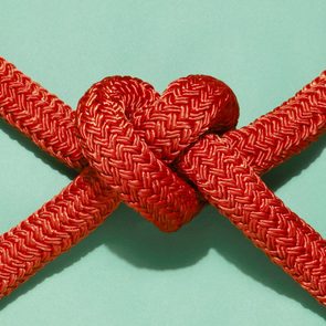 Red rope forms a knot against a light green background, with intricate weaves visible.