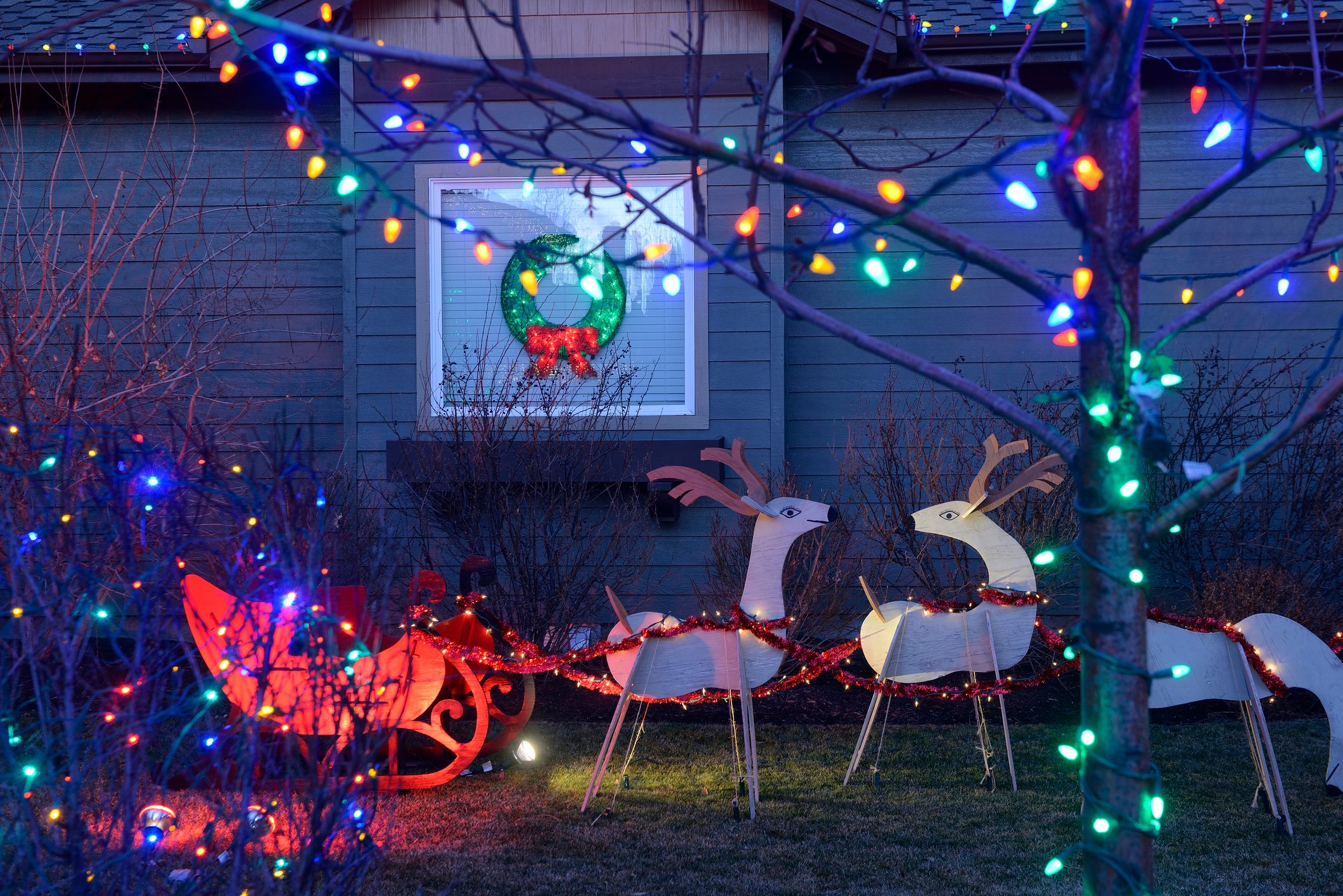 multicolored christmas lights and santas sleigh and reindeer holiday decor in a front yard of a house