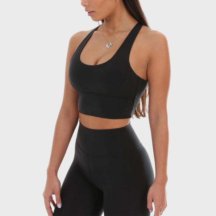 Woman stands, wearing a black sports outfit, looking sideways. White background focuses attention on clothing and posture.