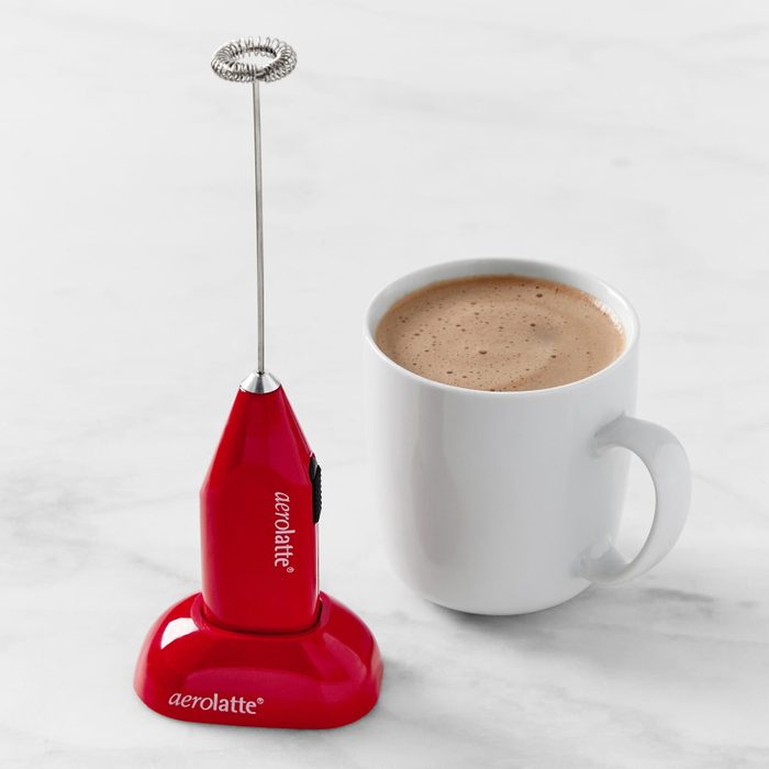 Frother rests on stand, next to a white mug of frothy coffee on a marble surface. Text reads â€œaerolatteâ€ on the frother.