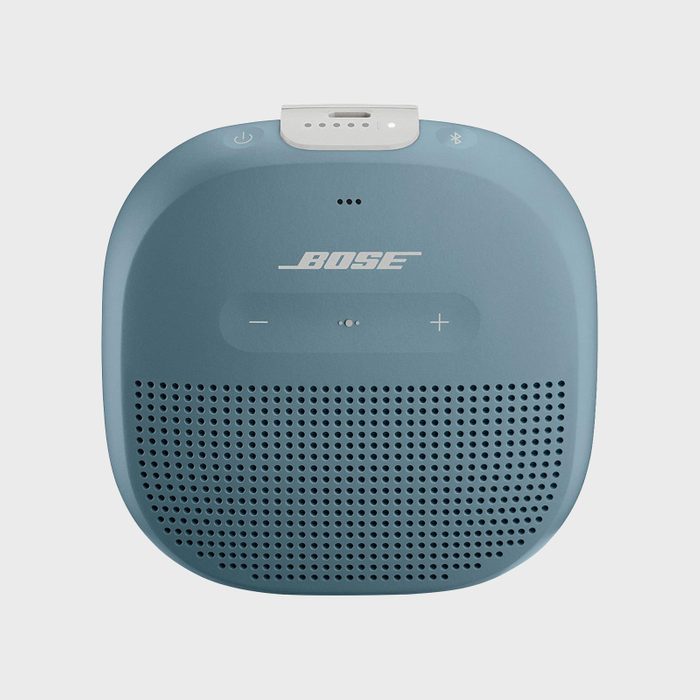 A compact, blue Bluetooth speaker sits idle, displaying volume controls and branding, against a plain white background.