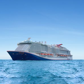 Cruise ship sails across open ocean under a clear blue sky, with visible text 