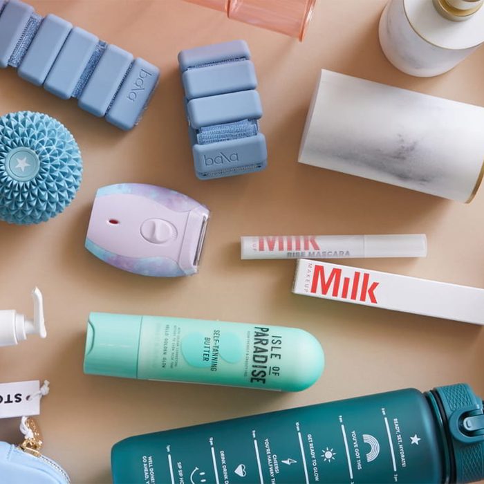 Various wellness and beauty products, including blue weights, skincare items, and makeup, are arranged neatly on a flat surface. The text includes 