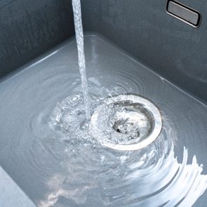 Water flows into a gray sink, swirling around the drain, creating ripples.
