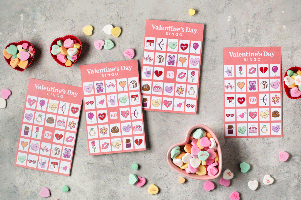 Bingo cards show Valentine's Day symbols; candy hearts sit in red and pink heart-shaped bowls on a textured gray surface.
