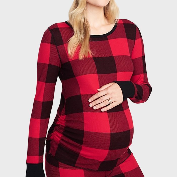A person wearing red plaid maternity pajamas, touching their belly with both hands gently, set against a plain light gray background.