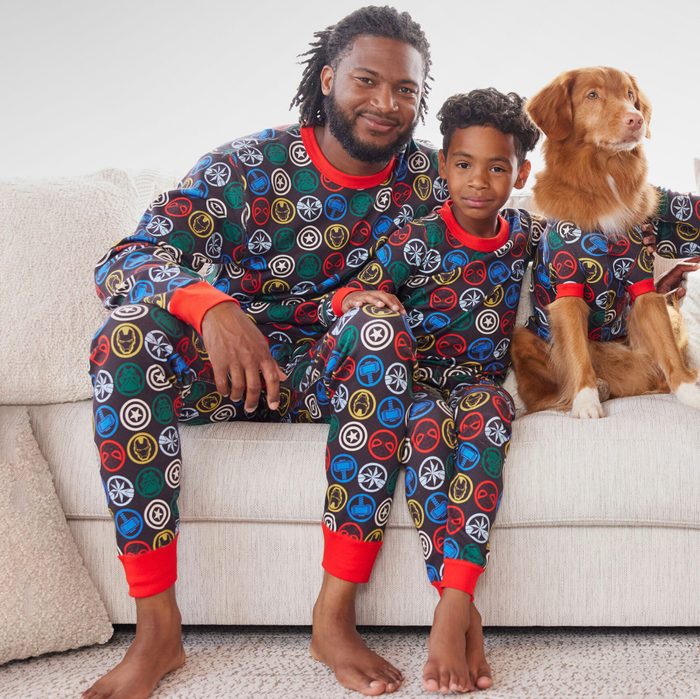 Three figures in matching superhero-themed pajamas sit together on a light-colored sofa.