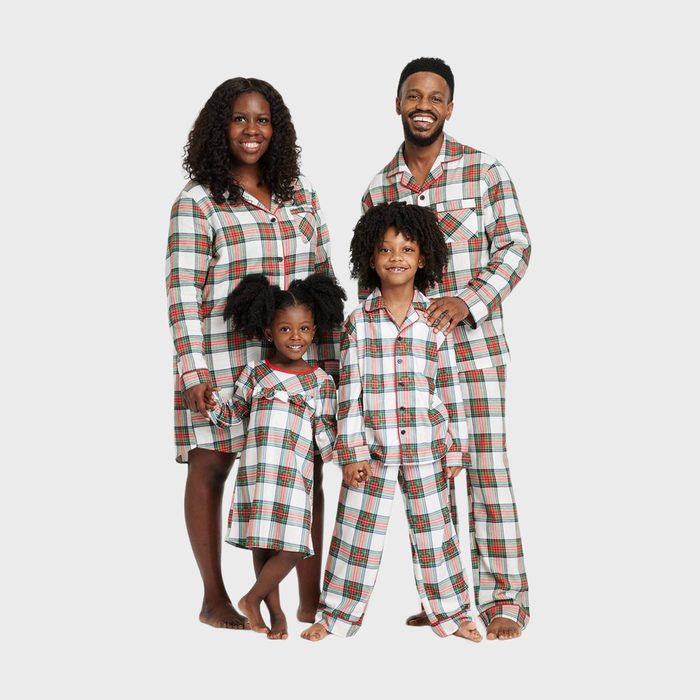 Family wearing matching plaid pajamas, standing together, smiling; against a plain white background.