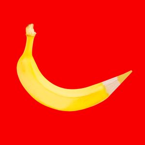 A banana-shaped object transforms into a pencil, set against a vibrant red background.