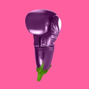 Boxing glove shaped like an eggplant sits centered against a solid pink background.