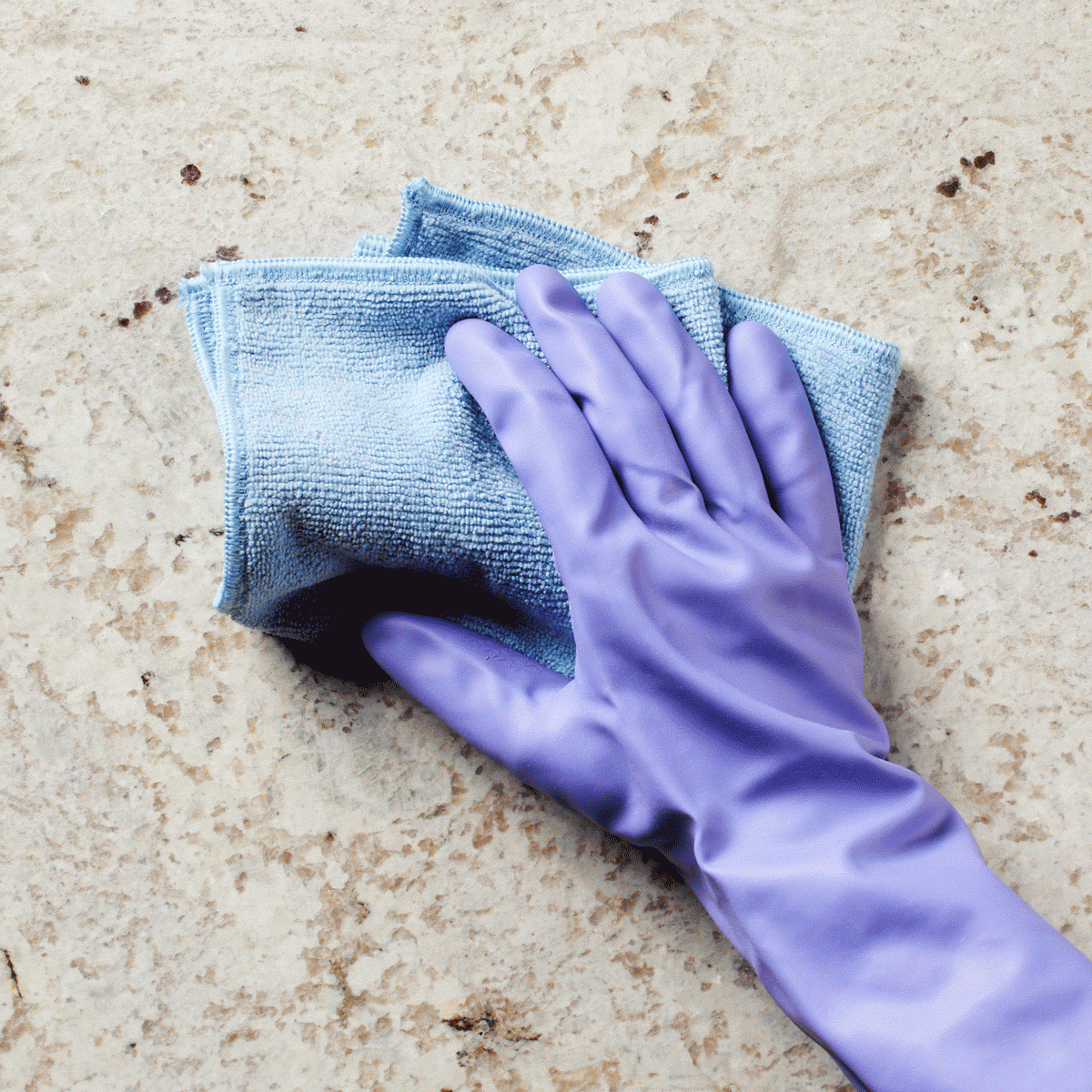 Purple-gloved hand wipes a marble surface with a blue microfiber cloth.