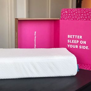 White pillow rests on a table, with an open pink box behind it displaying the text, 