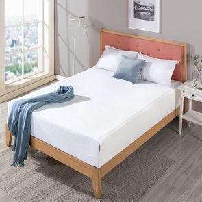 Bed with white bedding holds a blue throw, situated by a large window in a neutral-toned room featuring simple decor.