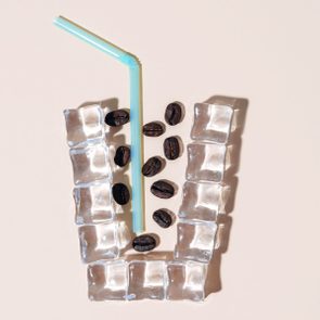 Ice cubes form a glass shape, coffee beans scattered inside, blue straw placed vertically, neutral background.