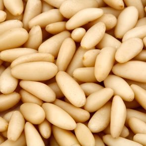Pine nuts scattered closely together, forming a textured pattern, with no additional background objects or text.