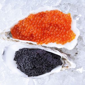 Oyster shells hold vibrant orange and black caviar, resting on a bed of ice.