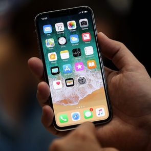 Hand holds smartphone, displaying home screen apps, in dim environment.