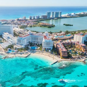 Beachfront hotels overlook turquoise ocean waters, with a boat sailing nearby, set within a vibrant coastal cityscape under a clear blue sky.