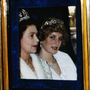 Two women sit in a carriage, wearing elegant tiaras and white fur coats, framed by a window with a blue and gold border.
