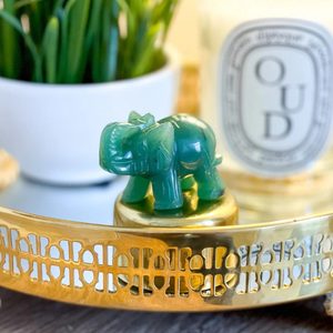 Green jade elephant statue stands on a gold surface, surrounded by a white plant pot and a candle labeled 