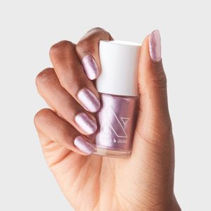 Hand holding pink nail polish bottle with nails painted, against a plain white background.