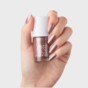 Hand holding a metallic nail polish bottle with painted nails, against a plain white background. The bottle reads 