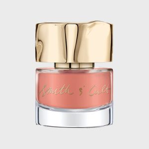 A glass nail polish bottle displays pink polish, featuring a gold cap and the text 