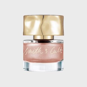 A nail polish bottle sits on a plain background with gold cap and 