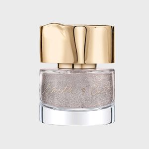 Metallic gold nail polish rests in a clear glass bottle with a shiny gold cap; 