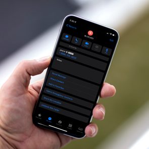 Hand holds a smartphone displaying a blocked contact screen with call and message options outdoors.