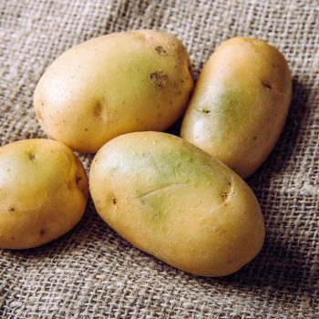 Four potatoes lie scattered on a textured burlap fabric.