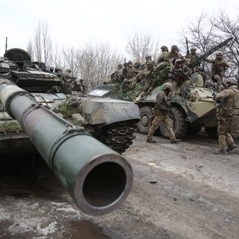 Tank stationed; soldiers gather on armored vehicle; winter trees surround.