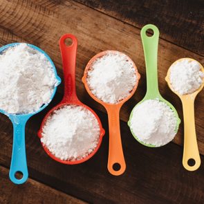 Colorful measuring cups hold flour, arranged in size order on a wooden surface.
