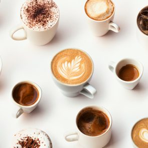 Various coffee cups displayed on a white surface, each with different styles and toppings, including froth designs and whipped cream.