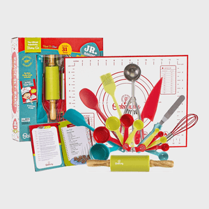 Baking kit displays colorful utensils and measuring tools arranged on a white mat, accompanied by a recipe booklet. Packaging box is visible in the background.