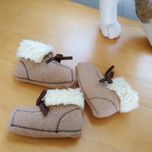 Three small, fluffy booties rest on a wooden table, near a white paw.