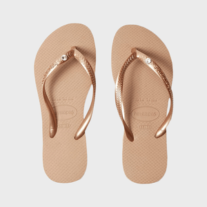 Sandals lie flat on a white surface, featuring metallic bronze straps with a decorative gem, brand name 