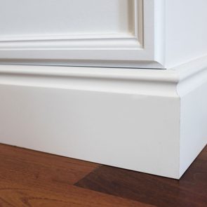 White baseboard meeting wooden floor, featuring a simple rectangular design, set against a smooth white wall background.