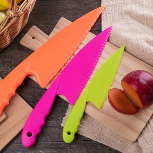 Colorful knives, resting on wooden boards, near halved red plum, with a cloth and basket of fruit nearby.