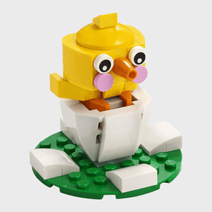 A yellow LEGO chick emerging from a cracked eggshell sits on a green LEGO base.