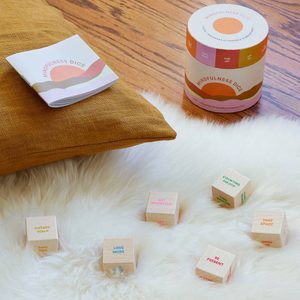 Wooden mindfulness dice rest on a fluffy surface; nearby are a pillow, booklet, and cylindrical container.