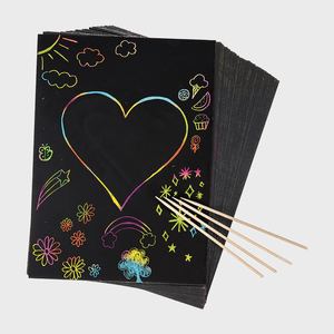Black scratch art paper displays colorful doodles using wooden stylus; includes a heart, clouds, stars, and ice cream within a creative setting.