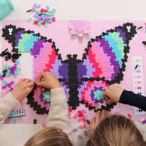 Hands assemble colorful puzzle pieces into a butterfly shape on a pink surface, surrounded by scattered pieces and a color guide.