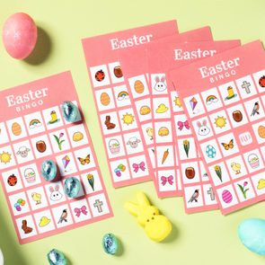 Bingo cards lie on a green surface, covered with Easter-themed illustrations, surrounded by colorful eggs and candies.