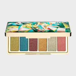 A makeup palette displays six shimmering eyeshadow colors in a gold case, adorned with a geometric, multicolored lid design. Text: 