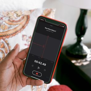 A hand holds a smartphone recording audio, displaying 