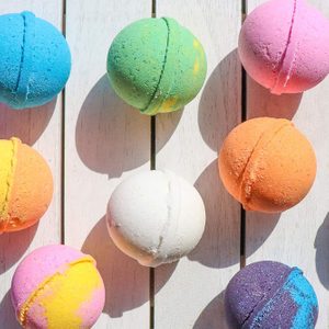 Colorful bath bombs rest on a white wooden surface, casting shadows.