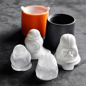 Silicone molds depicting characters rest on a dark surface, next to similar ice figures. An orange cup with a spout is in the background.