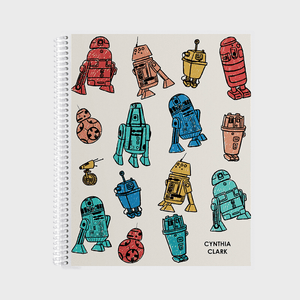 Colorful, cartoon robots are scattered on a spiral-bound notebook cover with a beige background. Text reads 